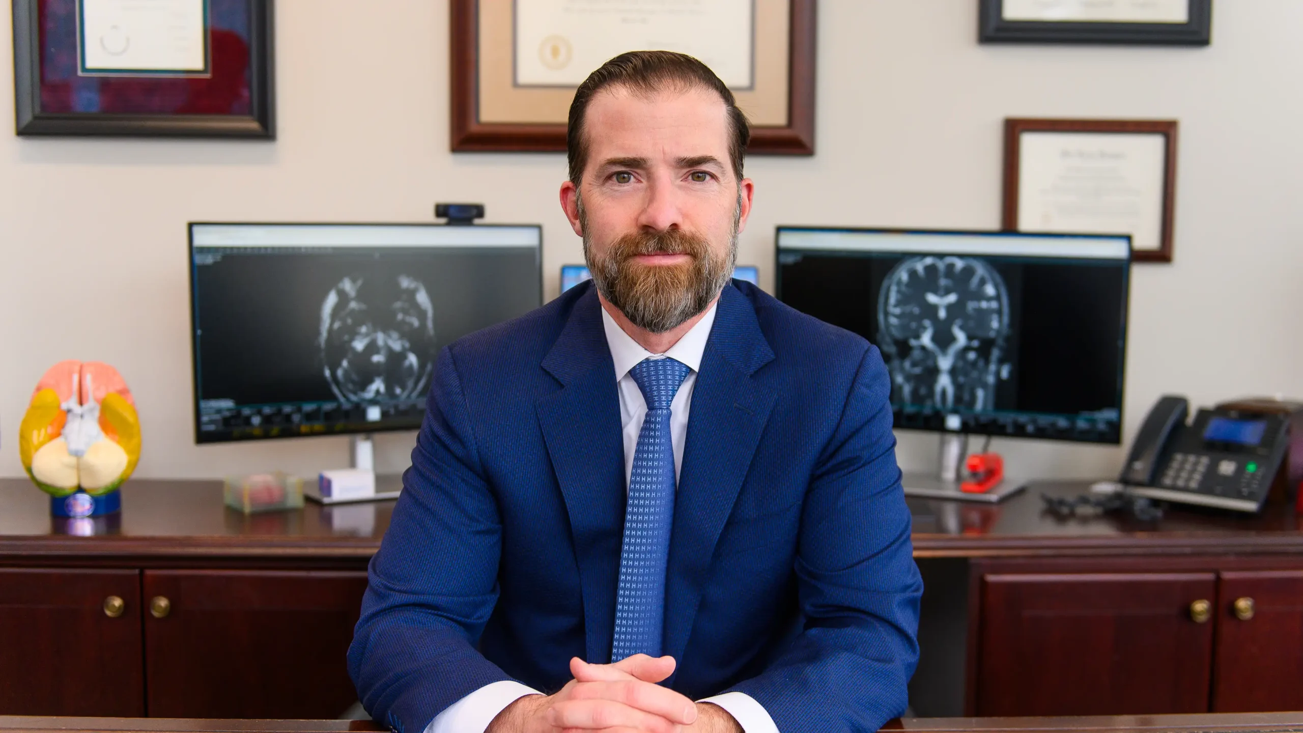 Expert Skull Base Fellowship Neurosurgeon Dr. Anthony D'Ambrosio sits at his desk in front of scans for a patient who presents with symptoms of Hemifacial Spasm