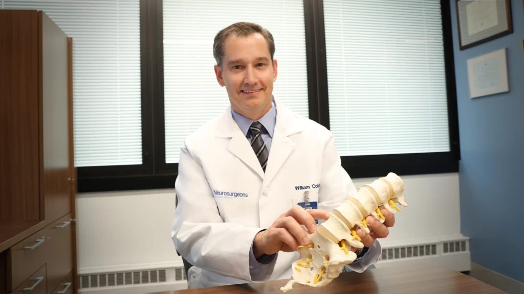 Dr. William Cobb Holding a Lumbar Spine Model, pointing at one of the vertebrae.