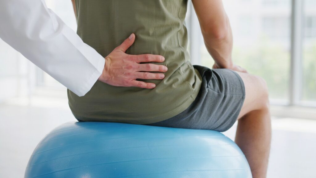 Physical therapist examining a patients lower back while sitting on an exercise ball.
