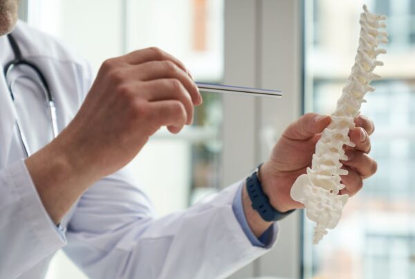 Doctor talking to a patient holding a model of a human spine.