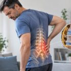 Middle aged man holding painful lower back region with highlighted herniated disc illustration.